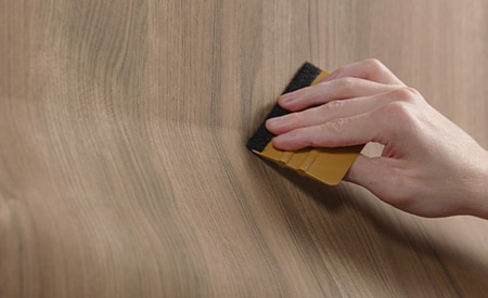 Primer plano de una herramienta de limpieza (escobilla de goma) siendo utilizada para instalar un acabado con patrón de madera.
