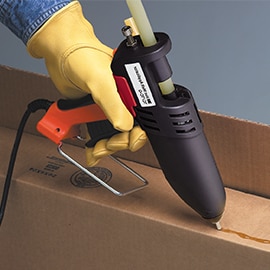 Hot melt adhesive is applied to the inside flap of a cardboard box