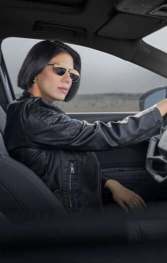 Mujer sentada en el asiento del conductor con lentes oscuros.
