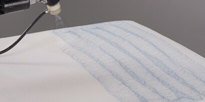 Image of an applicator spraying hot melt adhesive in a consistent side-to-side pattern on a large surface
