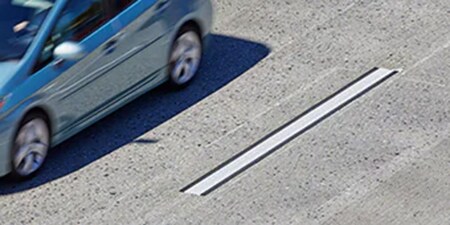 Un coche azul pasa rápidamente por una señalización vial de alto contraste que es fácilmente visible en el pavimento.
