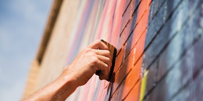Imagen de una mano usando una herramienta para instalar una película gráfica impresa en una pared de ladrillos.
