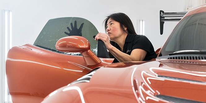 Woman installing window tint on interior passenger side window on sports car
