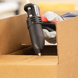 Hot melt adhesive is applied to the top of a cardboard box