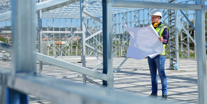 Dos trabajadores con chalecos de alta visibilidad y cascos están en una instalación industrial luminosa rodeados de grandes tuberías, válvulas y equipos de procesamiento.