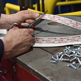 Image of a someone in a manufacturing setting using scissors to cut a strip from a roll of 3M™ Dual Lock™