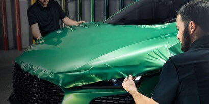 Dos hombres instalando una película de color verde esmeralda sobre el capot de un coche deportivo.
