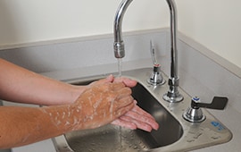 close up of soapy hands being washed with hot water under a commercial sink