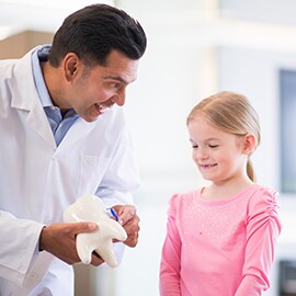 White male doctor showing white little girl in pink how to use a tooth brush on a oversized cartoon-like tooth
