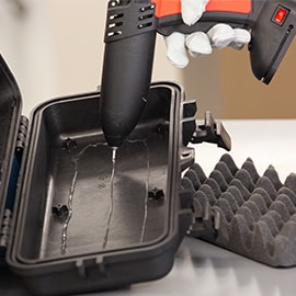 Hot melt adhesive is applied to the inside of a black carton