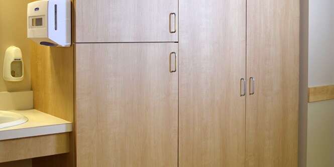 Imagen del fregadero y el gabinete de almacenamiento en una habitación de hospital que fue renovada con película arquitectónica 3M DI-NOC en tonos de madera clara.

