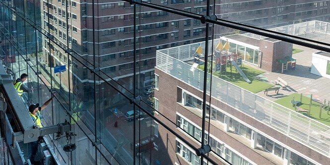 Trabajadores en andamios instalando películas para ventanas en una fachada de vidrio.
