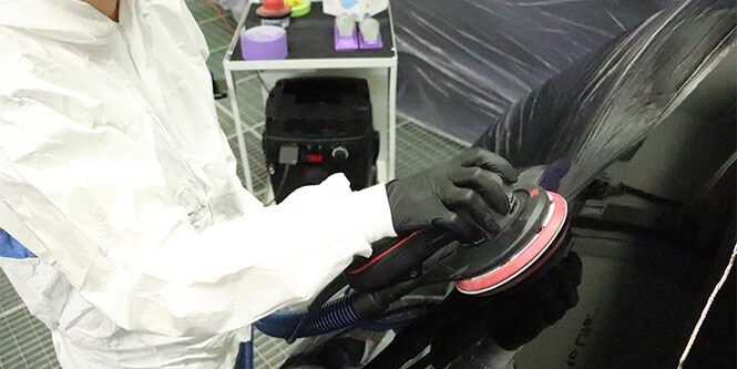 Trabajador en un taller utilizando una lijadora del Sistema de Lijado Limpio de 3M en la superficie de un vehículo.

