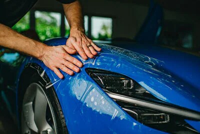 Detalle de un técnico que aplica una película protectora de pintura PPF 3M a un automóvil.