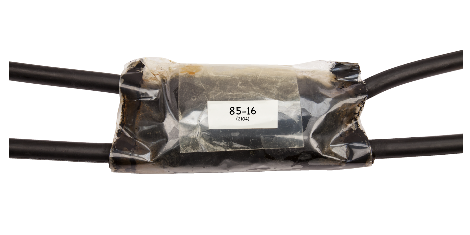 Kit de empalme de derivación eléctrico envuelta en material aislante transparente con etiqueta “85-16”, uniendo dos cables negros.
