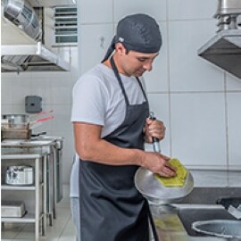 Un trabajador de cocina comercial frota una sartén en un fregadero.