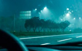 Imagen de la vista desde dentro de un coche mirando directamente hacia la carretera, es de noche y está lloviendo, y hay cinta reflectante en la carretera.